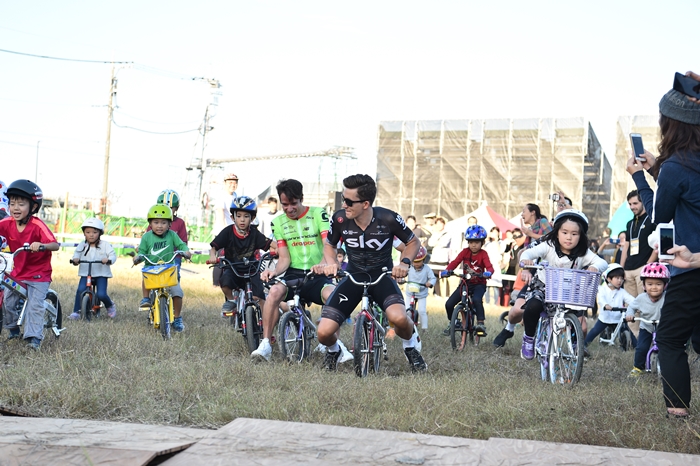広場では子供達が自転車走行体験。海外選手達も楽しげに混じっ…
