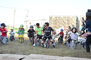広場では子供達が自転車走行体験。海外選手達も楽しげに混じっている。