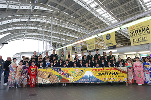 和装をした海外選手達と岩槻商業高校書道部の生徒達、岩槻黒奴の皆さん、和装で出迎えたさいたま市役所職員達でさいたま新都心駅にて集合写真を撮影